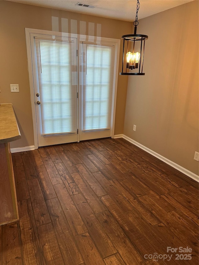 unfurnished dining area with dark wood-style floors, a chandelier, and baseboards