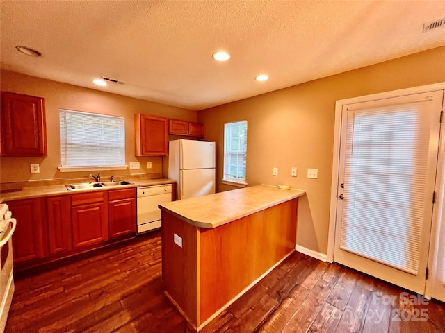 kitchen featuring white appliances, a sink, a peninsula, dark wood-type flooring, and light countertops