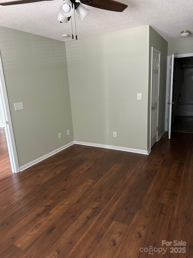 empty room featuring a ceiling fan, a textured ceiling, dark wood-type flooring, and baseboards