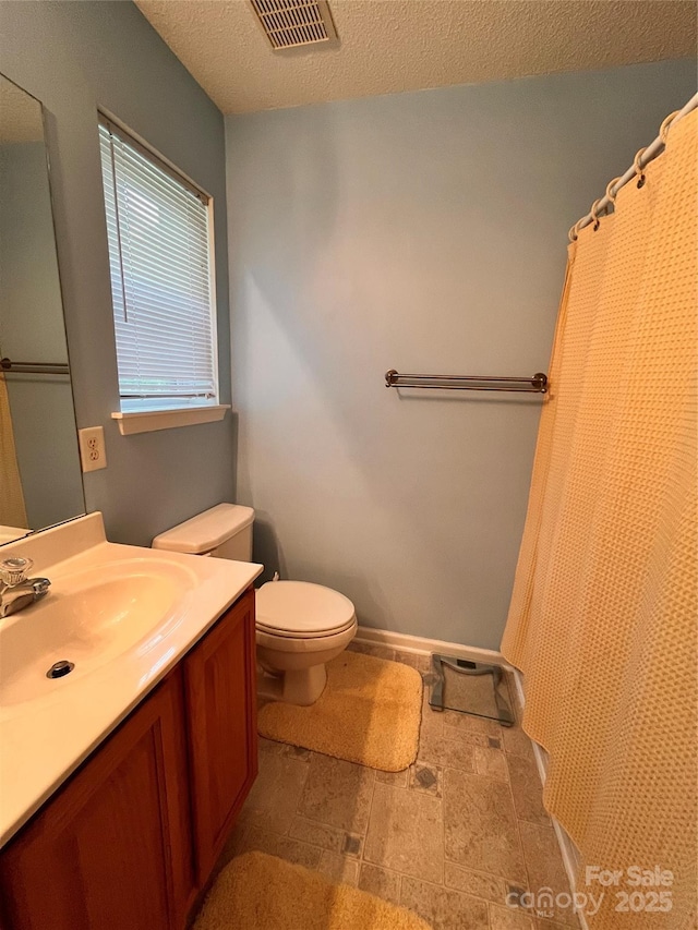 bathroom with toilet, vanity, stone finish floors, and a textured ceiling