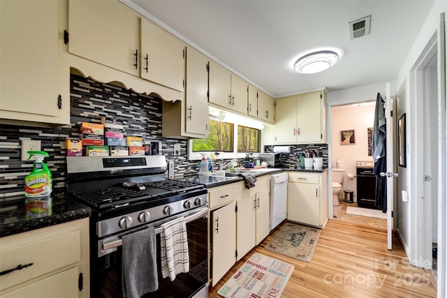 kitchen featuring gas stove, light hardwood / wood-style flooring, white dishwasher, cream cabinetry, and decorative backsplash