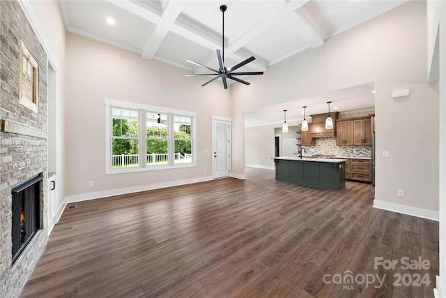 unfurnished living room with dark wood-type flooring, sink, crown molding, ceiling fan, and a large fireplace