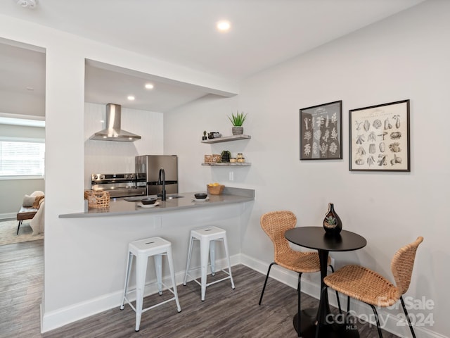 kitchen with appliances with stainless steel finishes, wall chimney exhaust hood, dark hardwood / wood-style flooring, sink, and a breakfast bar area