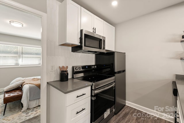 kitchen with appliances with stainless steel finishes, dark hardwood / wood-style flooring, and white cabinets