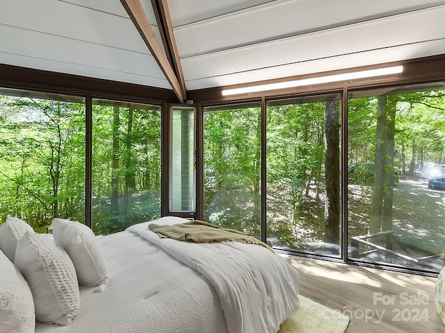 bedroom with wood-type flooring, beam ceiling, and multiple windows