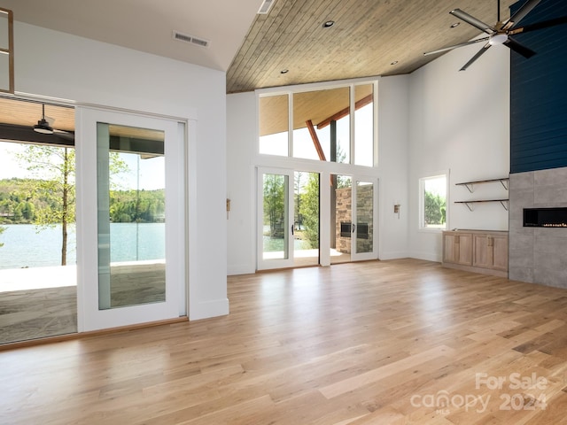 unfurnished living room featuring ceiling fan, wood ceiling, light hardwood / wood-style flooring, a tile fireplace, and a towering ceiling