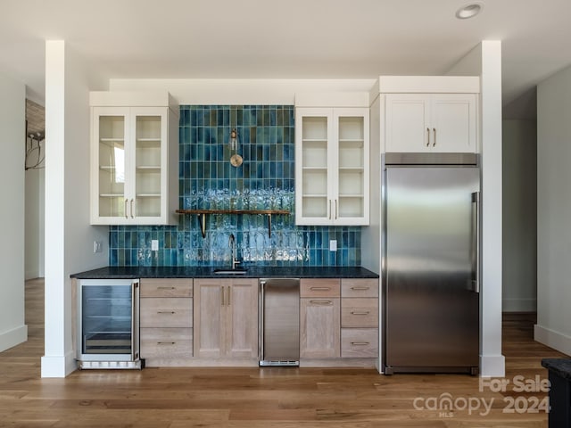 bar with stainless steel built in refrigerator, sink, beverage cooler, hardwood / wood-style flooring, and light brown cabinetry