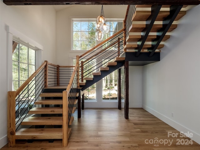 stairway with an inviting chandelier, wood-type flooring, and a healthy amount of sunlight