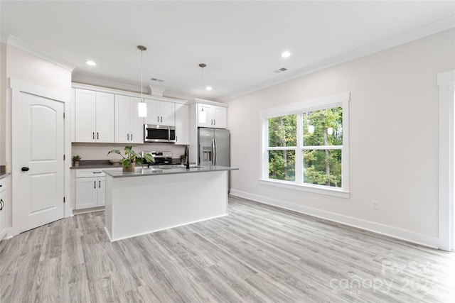 kitchen with light wood-type flooring, a kitchen island with sink, white cabinetry, appliances with stainless steel finishes, and decorative light fixtures