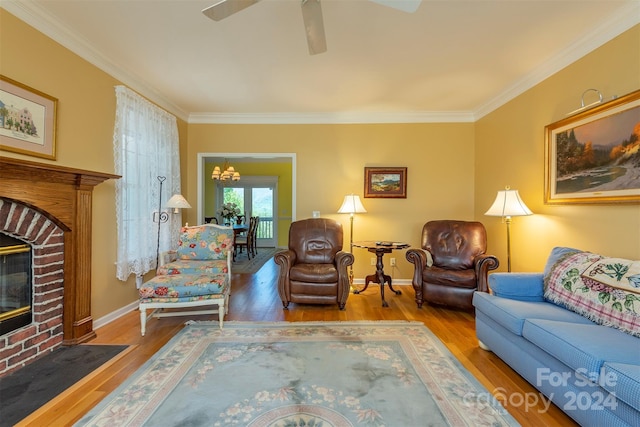 living room featuring hardwood / wood-style floors, ornamental molding, ceiling fan with notable chandelier, and a brick fireplace