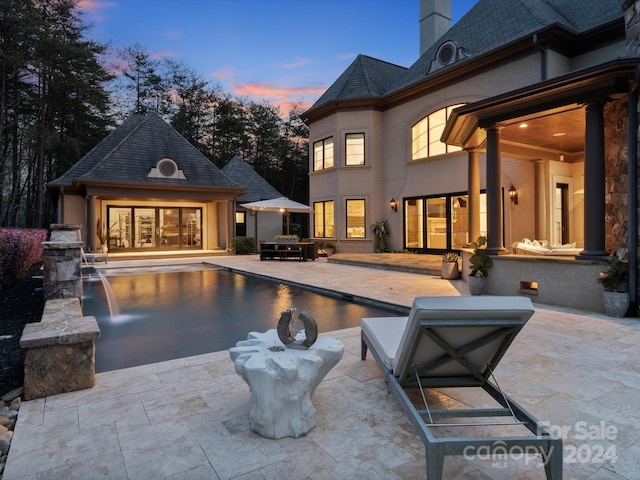 back house at dusk with pool water feature and a patio