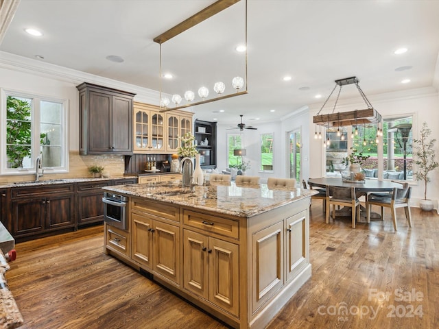 kitchen with sink, ornamental molding, hardwood / wood-style flooring, and a kitchen island with sink