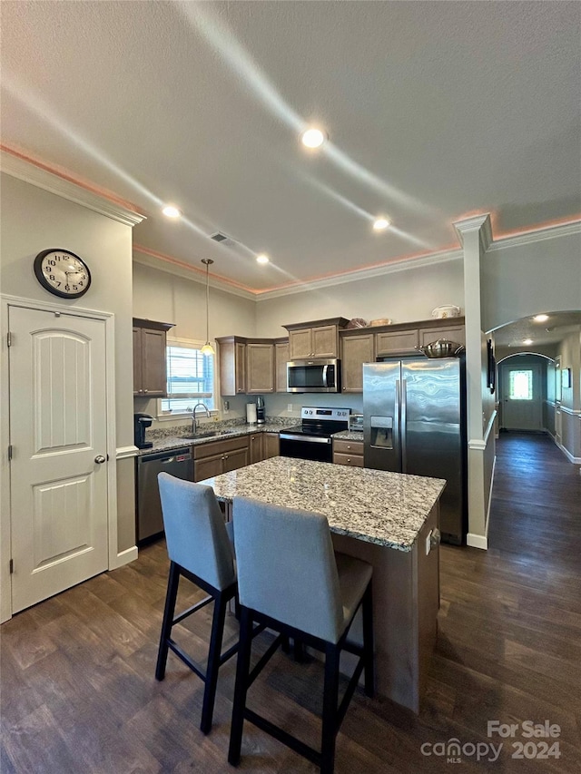 kitchen featuring appliances with stainless steel finishes, a kitchen island, hanging light fixtures, dark hardwood / wood-style flooring, and ornamental molding