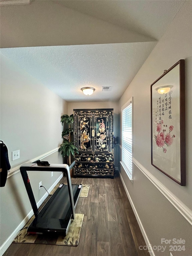 exercise room featuring a textured ceiling, dark hardwood / wood-style flooring, and vaulted ceiling