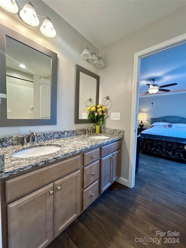 bathroom featuring wood-type flooring, ceiling fan, vanity with extensive cabinet space, and dual sinks