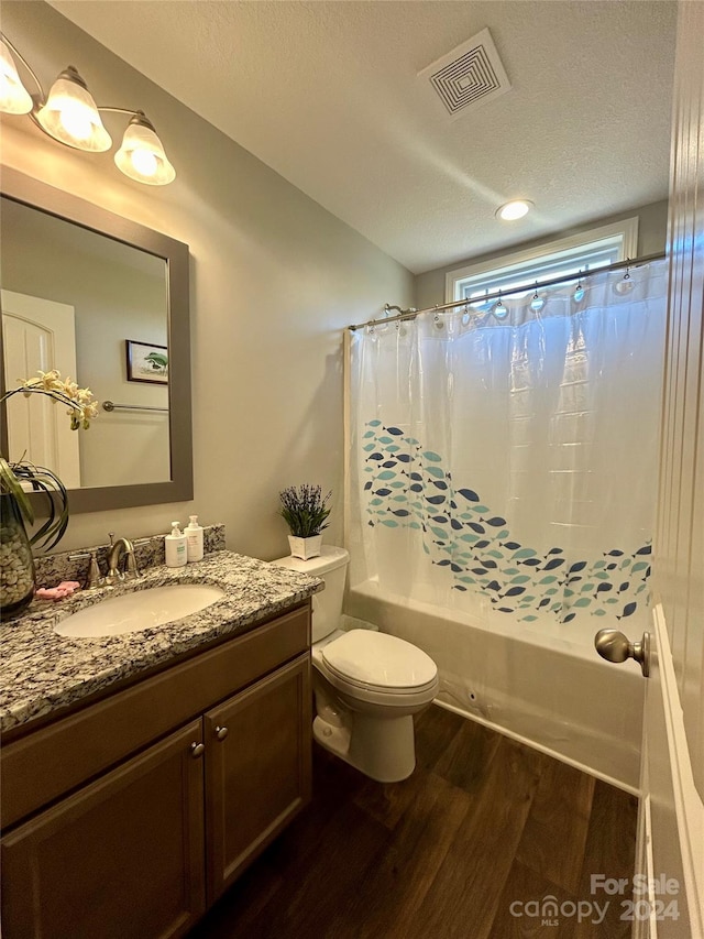 full bathroom with a textured ceiling, oversized vanity, shower / tub combo, toilet, and wood-type flooring