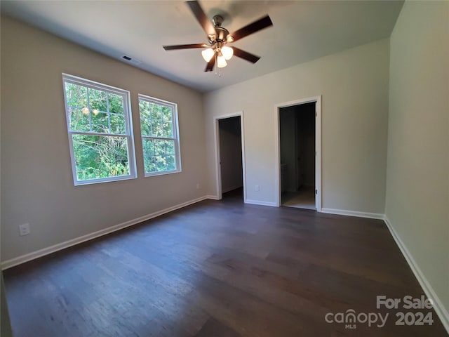 unfurnished bedroom with ensuite bath, a spacious closet, dark hardwood / wood-style floors, and ceiling fan