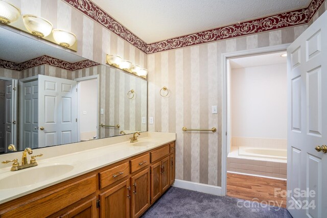 bathroom with double sink vanity, a textured ceiling, a relaxing tiled tub, and hardwood / wood-style floors