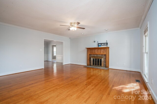 unfurnished living room with crown molding, a textured ceiling, a brick fireplace, ceiling fan, and light hardwood / wood-style floors