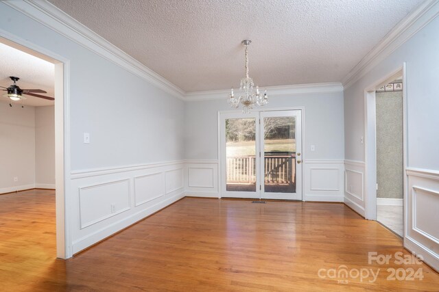 unfurnished dining area with wood-type flooring, ceiling fan with notable chandelier, a textured ceiling, and crown molding