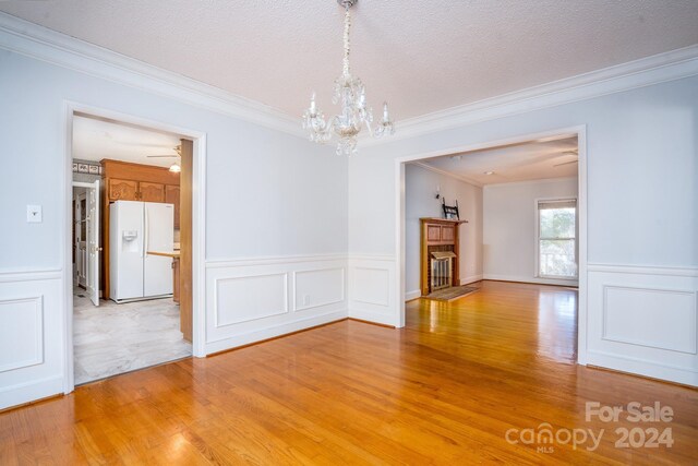 spare room featuring light hardwood / wood-style flooring, a textured ceiling, crown molding, and ceiling fan with notable chandelier