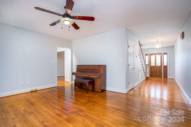 unfurnished living room with ceiling fan with notable chandelier, wood-type flooring, and a textured ceiling