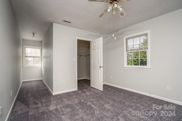 unfurnished bedroom featuring ceiling fan, a walk in closet, a textured ceiling, and carpet