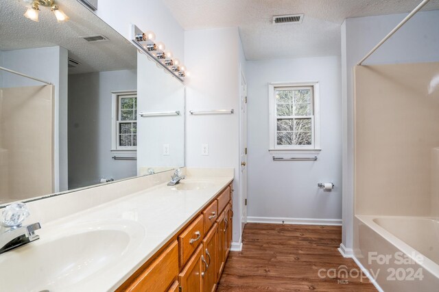 bathroom featuring tub / shower combination, a textured ceiling, dual bowl vanity, and hardwood / wood-style flooring