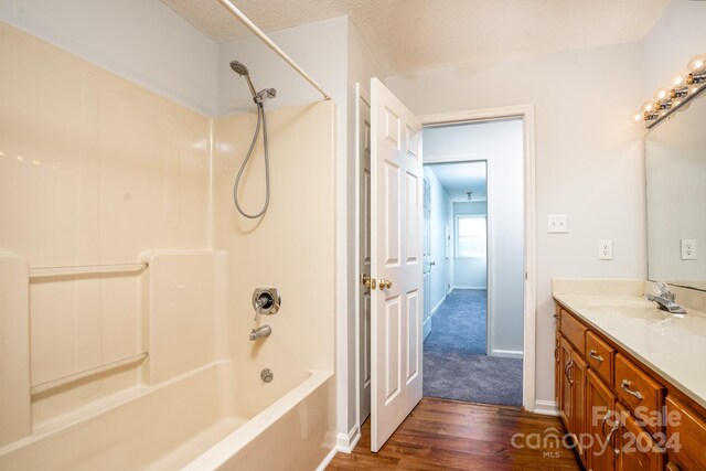 bathroom with a textured ceiling, vanity,  shower combination, and hardwood / wood-style floors