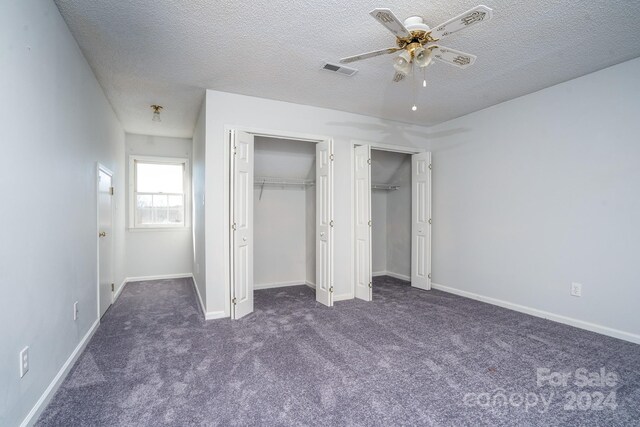 unfurnished bedroom featuring ceiling fan, a textured ceiling, dark carpet, and multiple closets