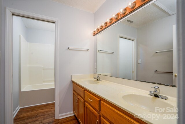 bathroom with shower / bath combination, wood-type flooring, a textured ceiling, and dual vanity