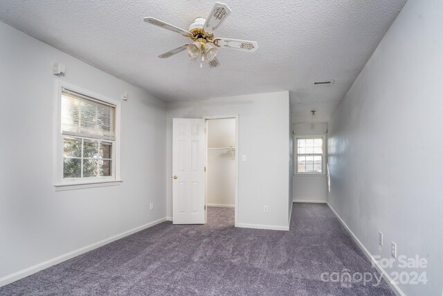 unfurnished bedroom featuring a textured ceiling, ceiling fan, a walk in closet, carpet flooring, and a closet