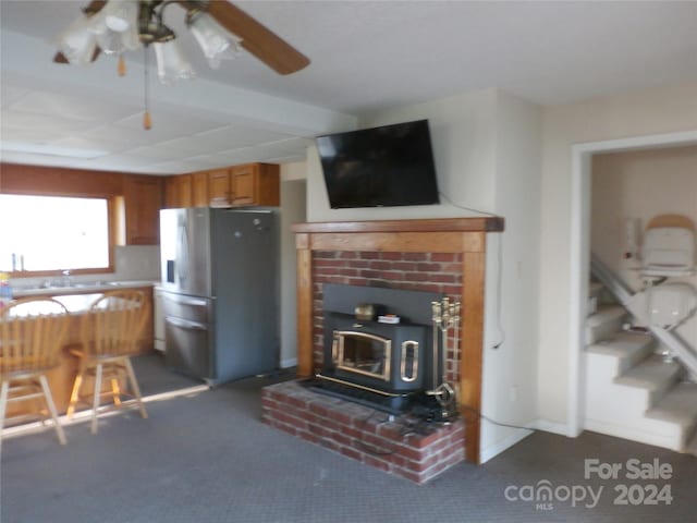 unfurnished living room with a wood stove, dark carpet, a fireplace, sink, and ceiling fan