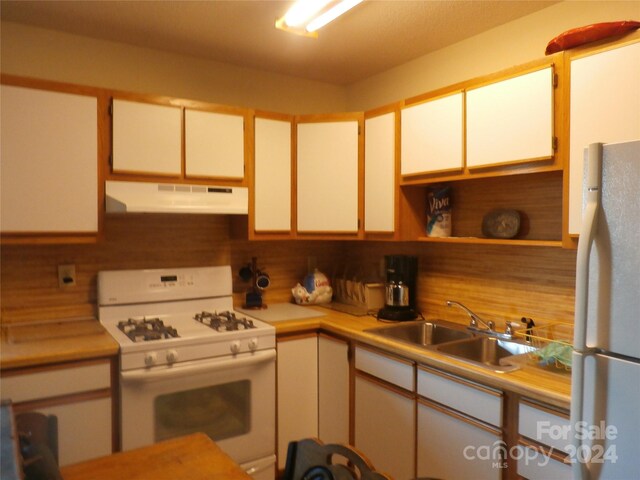 kitchen featuring sink, stainless steel refrigerator, tasteful backsplash, white cabinetry, and white gas range