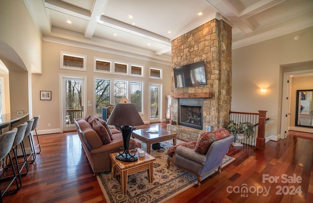 living room with beamed ceiling, ornamental molding, dark wood-type flooring, a fireplace, and a towering ceiling