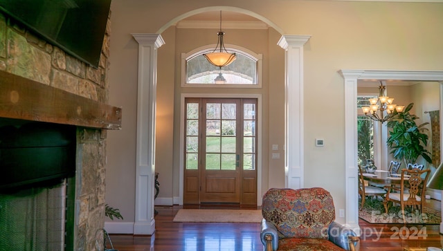 foyer entrance featuring decorative columns, ornamental molding, an inviting chandelier, and dark wood-type flooring