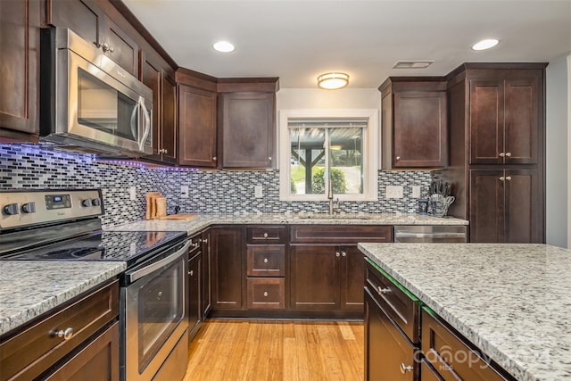 kitchen with sink, backsplash, light wood-type flooring, stainless steel appliances, and light stone countertops