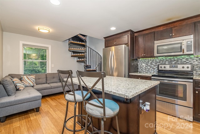 kitchen with a kitchen bar, light hardwood / wood-style flooring, stainless steel appliances, tasteful backsplash, and a center island