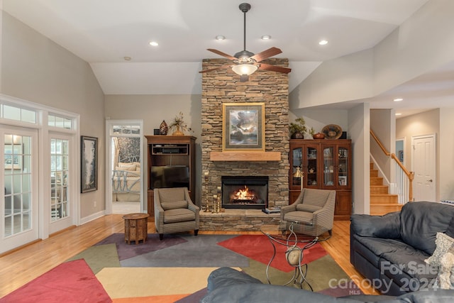 living room with ceiling fan, light hardwood / wood-style flooring, a stone fireplace, and high vaulted ceiling