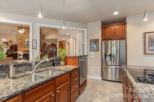 kitchen with appliances with stainless steel finishes, sink, dark stone countertops, and pendant lighting