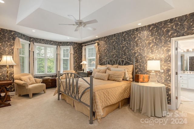 bedroom with ceiling fan, light colored carpet, connected bathroom, and a tray ceiling