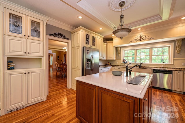 kitchen with decorative light fixtures, stainless steel appliances, a center island with sink, a tray ceiling, and hardwood / wood-style floors