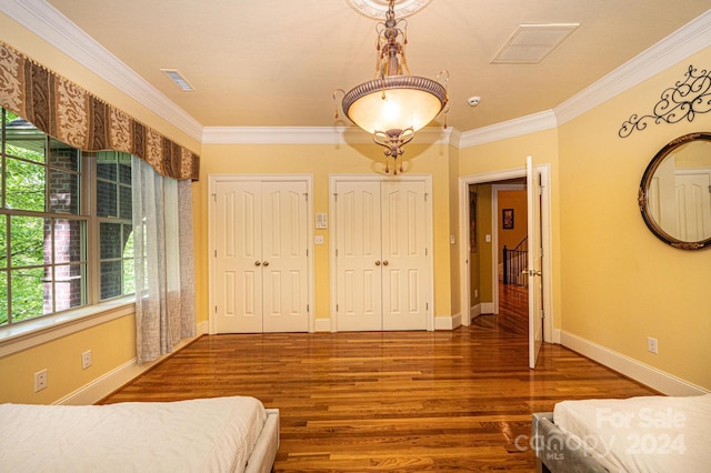 unfurnished bedroom with hardwood / wood-style flooring, ornamental molding, and two closets