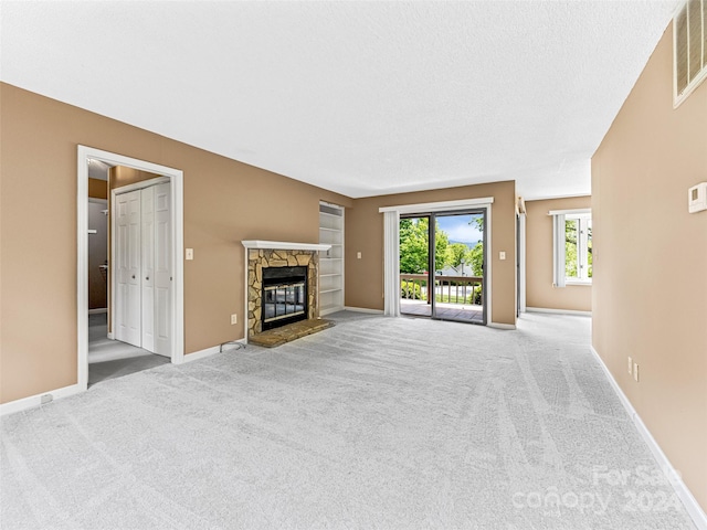 unfurnished living room with carpet, a textured ceiling, and a stone fireplace