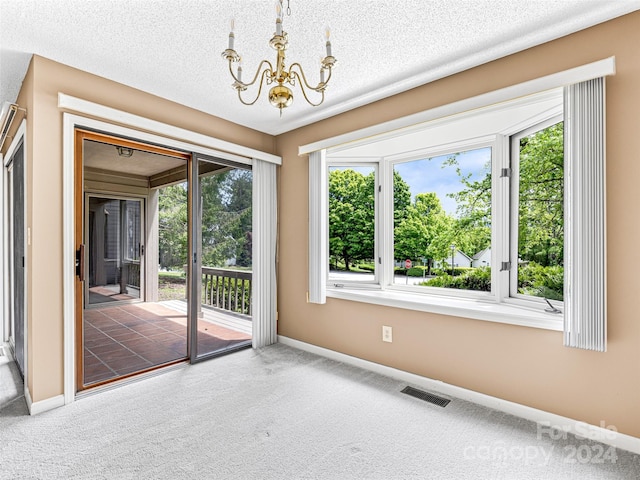 carpeted empty room with a wealth of natural light, an inviting chandelier, and a textured ceiling