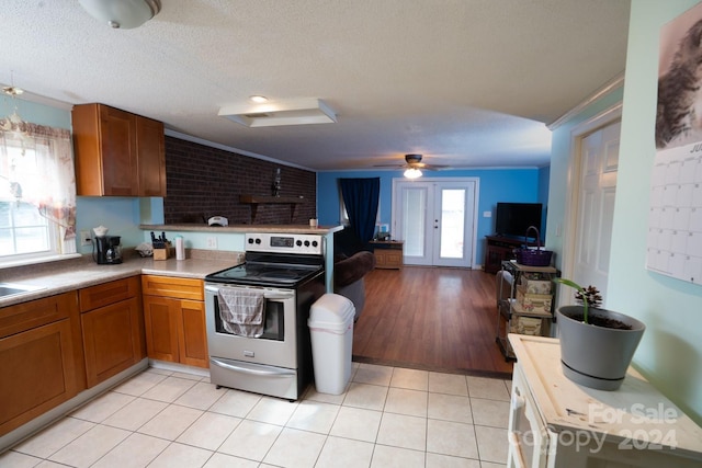 kitchen with a textured ceiling, light tile patterned flooring, crown molding, and stainless steel electric range