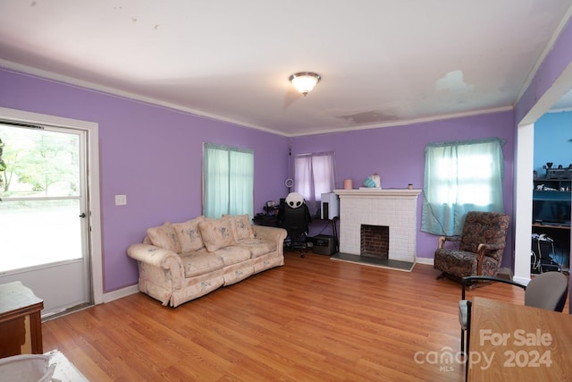 living room with light wood-type flooring, a wealth of natural light, ornamental molding, and a brick fireplace