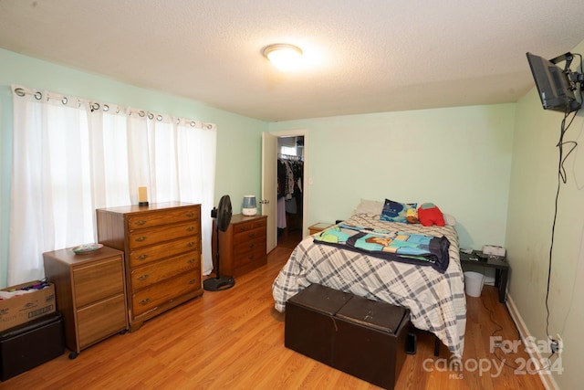 bedroom with a spacious closet, a closet, a textured ceiling, and light hardwood / wood-style floors