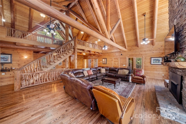 living room with wooden walls, wood-type flooring, high vaulted ceiling, a fireplace, and ceiling fan