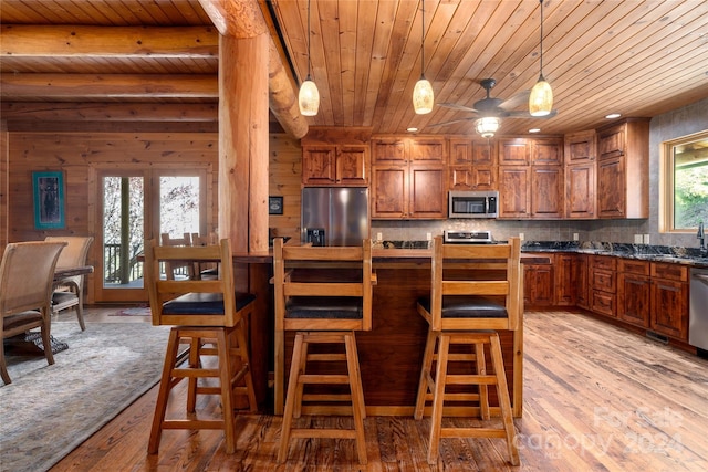 kitchen with wooden walls, pendant lighting, light hardwood / wood-style flooring, appliances with stainless steel finishes, and wood ceiling